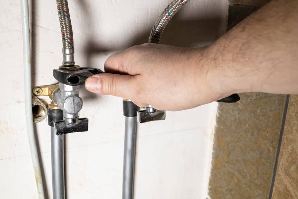 plumber hand installs water stop tap by adjustable wrench at home